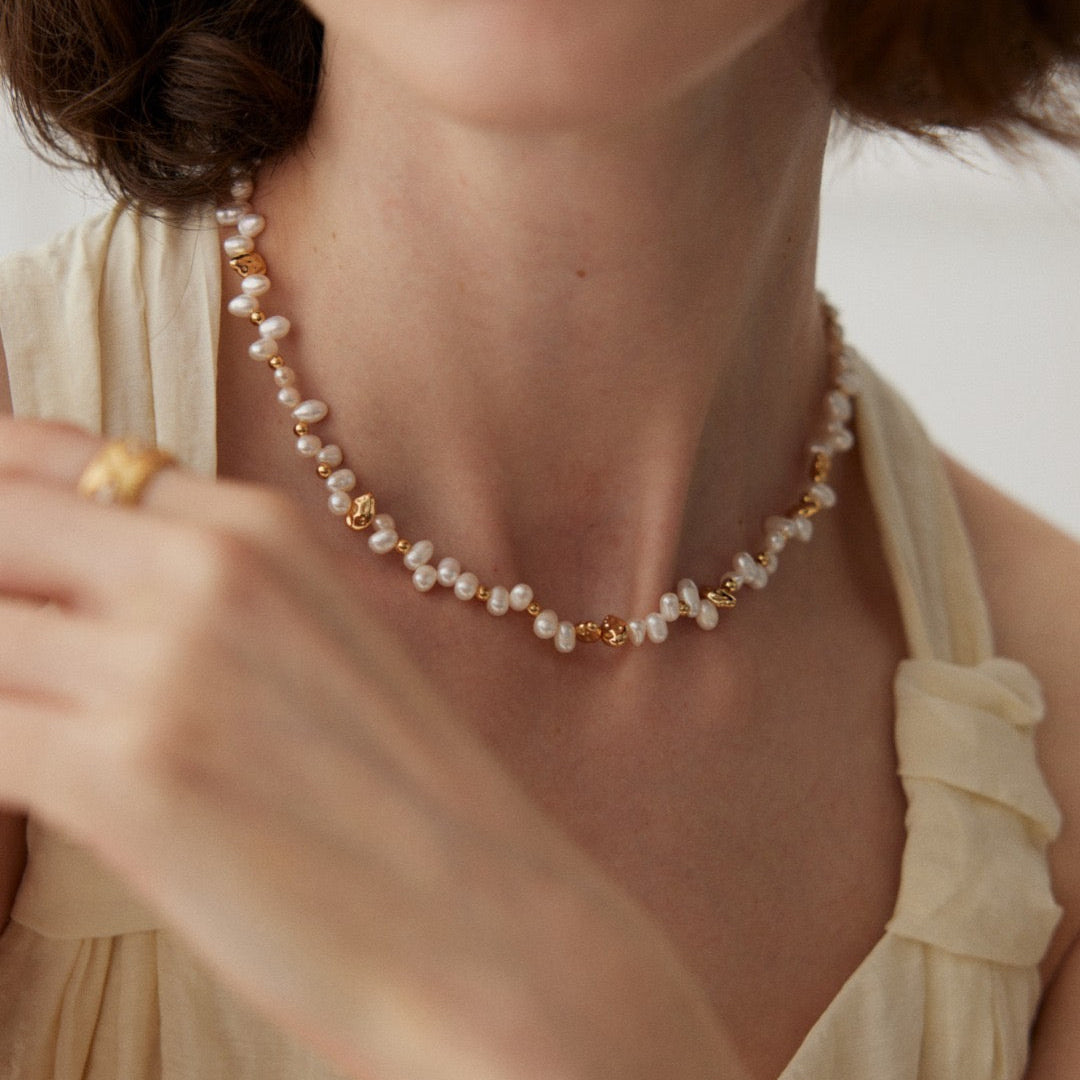 Pearl and gold-tone bead necklace worn with a light-coloured blouse